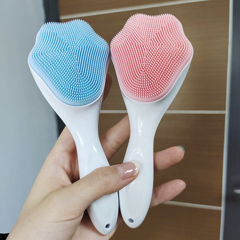 A hand holding blue and pink handheld silicone face scrubber exfoliators