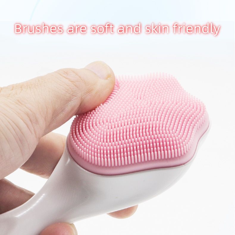 A finger touching the brush head on a pink handheld silicone face scrubber exfoliator