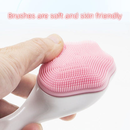 A finger touching the brush head on a pink handheld silicone face scrubber exfoliator